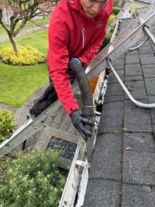 GutterVac technician on roof vacuuming gutters with long hose connected to ground vacuum unit