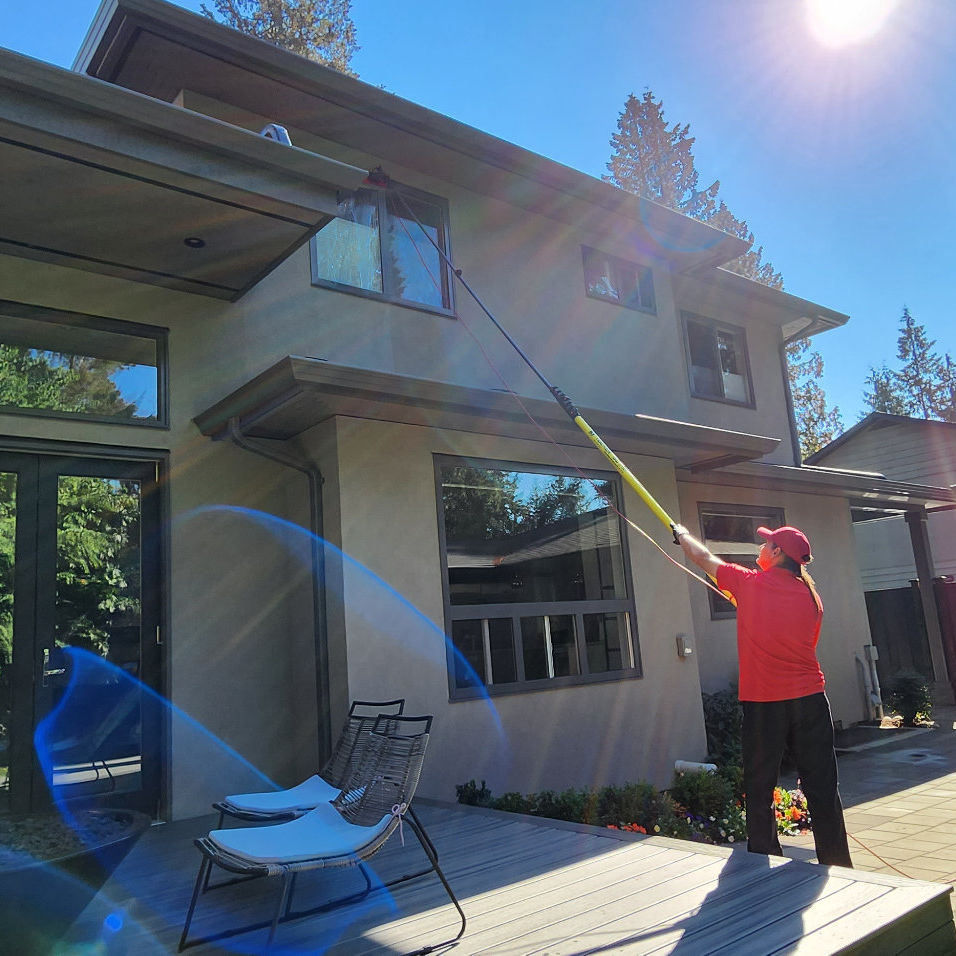 Guttervac team member cleaning upper floor windows on house